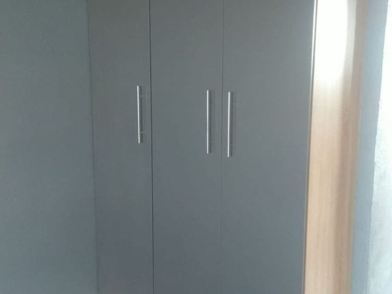 A bedroom featuring a modern, full-height built-in wardrobe with grey doors and wood-look trim.