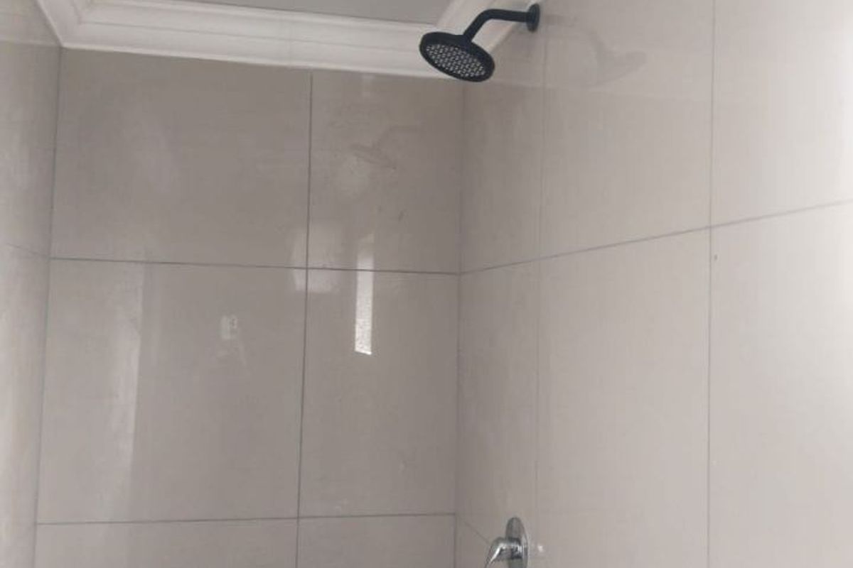 A clean, modern shower enclosure featuring neutral wall tiles, a contemporary black shower head, and chrome mixer tap.