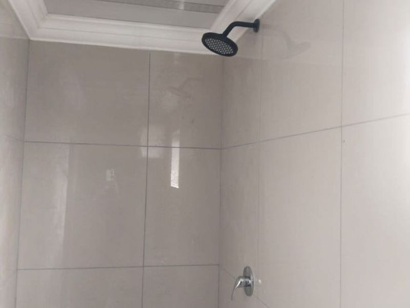A clean, modern shower enclosure featuring neutral wall tiles, a contemporary black shower head, and chrome mixer tap.