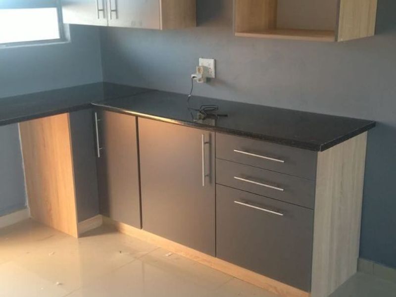 A modern, empty kitchen featuring dark grey and wood-tone cabinetry, granite countertops, and neutral tiled flooring.