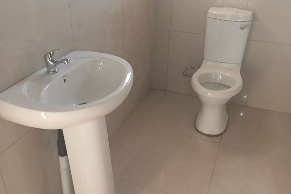 A clean, minimalist bathroom featuring a pedestal basin with a chrome mixer tap and a standard ceramic toilet, finished with neutral wall and floor tiles.