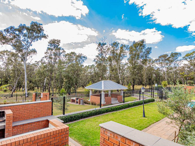 Outdoor communal area featuring a built-in brick braai, paved patio, swimming pool, and a covered gazebo set within a landscaped garden.