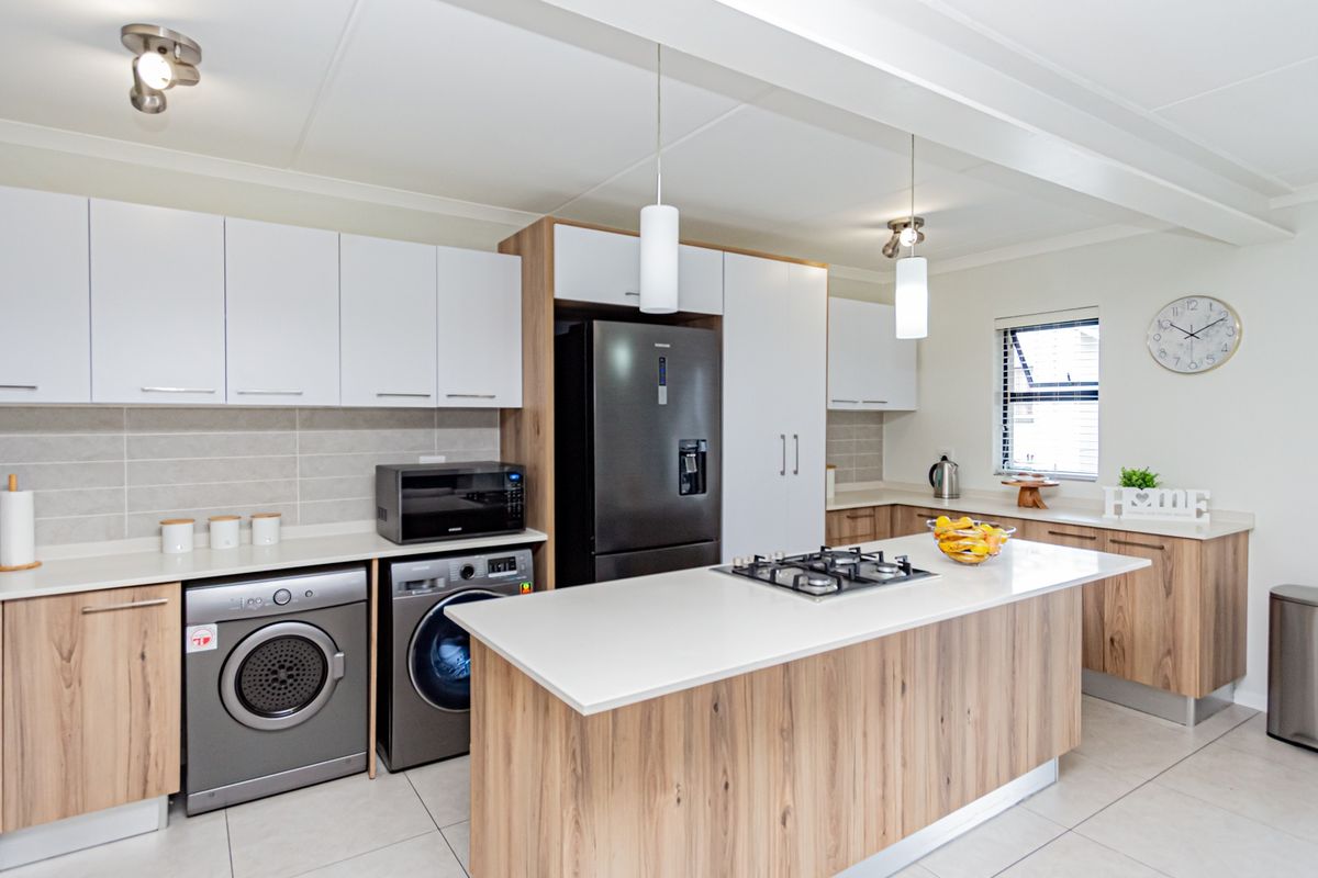 Modern kitchen featuring wood-grain and white cabinetry, stone countertops, a central island with a gas hob, and integrated appliances.