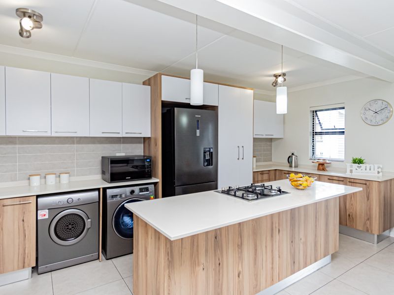 Modern kitchen featuring wood-grain and white cabinetry, stone countertops, a central island with a gas hob, and integrated appliances.