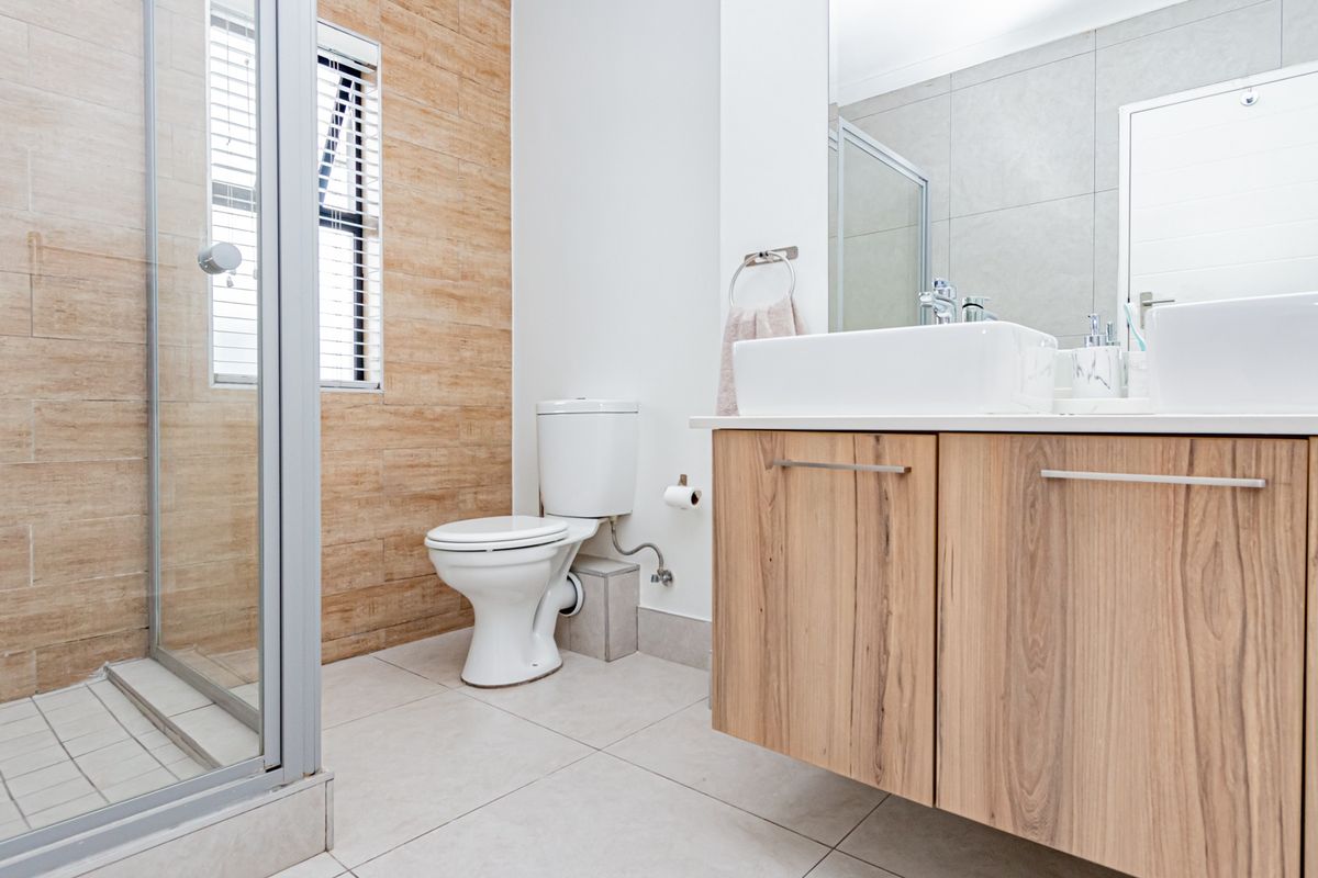 Modern bathroom featuring a walk-in shower, floating vanity with dual basins, and contemporary wood-look wall tiling.