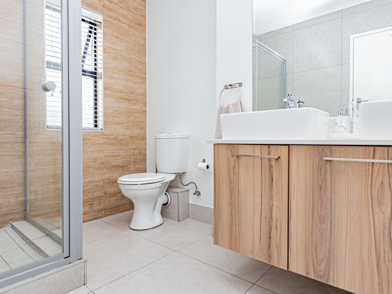 Modern bathroom featuring a walk-in shower, floating vanity with dual basins, and contemporary wood-look wall tiling.
