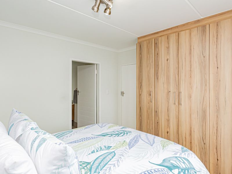 A bright bedroom featuring light wood-finish built-in wardrobes and a modern ceiling spotlight fixture.
