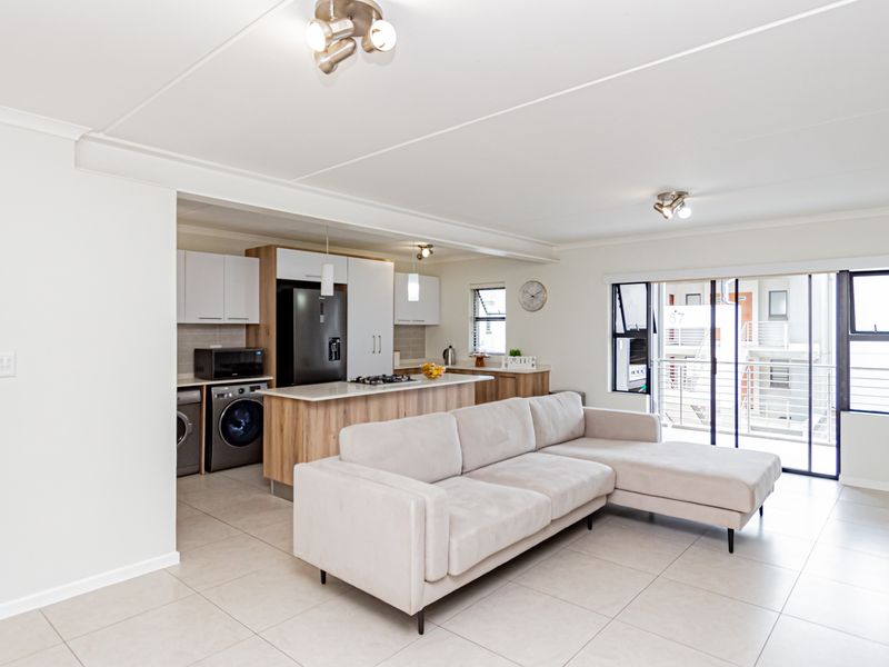Modern open-plan living area featuring a contemporary kitchen with a central island, tiled floors, and sliding doors leading to a balcony.