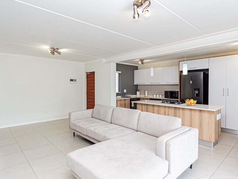 Modern open-plan living area featuring a contemporary kitchen with a central island, sleek cabinetry, and tiled flooring throughout.