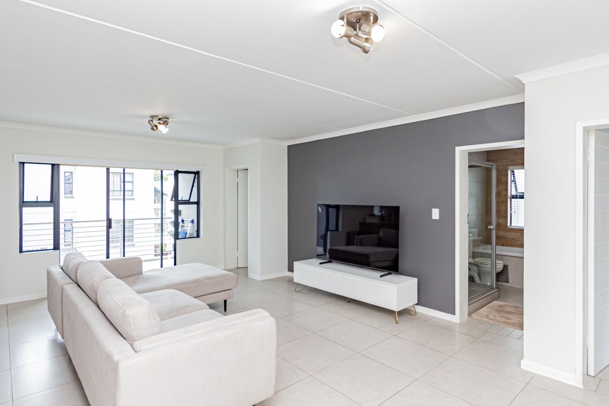 Bright and modern living room featuring neutral tiled flooring, a striking grey accent wall, and direct access to a balcony through sliding glass doors.