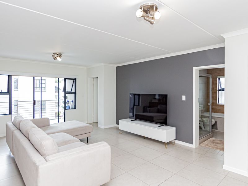 Bright and modern living room featuring neutral tiled flooring, a striking grey accent wall, and direct access to a balcony through sliding glass doors.