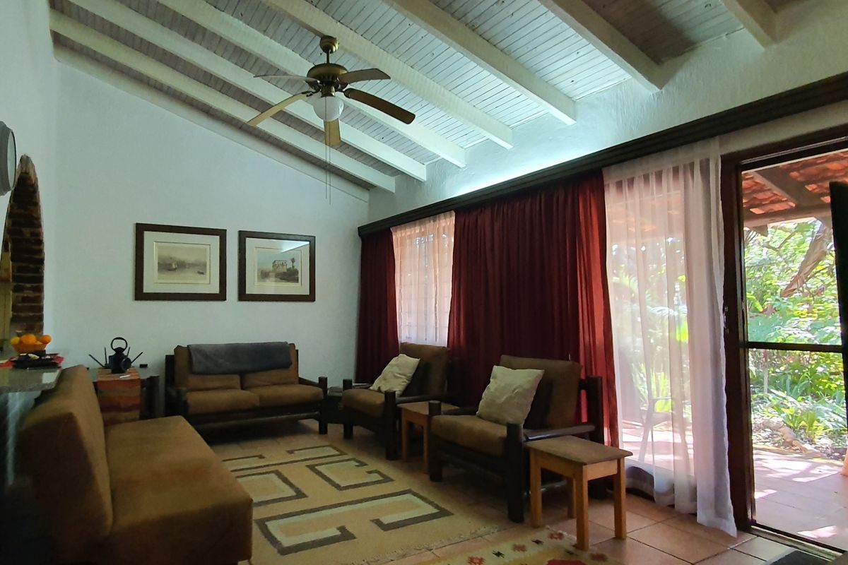 Living room featuring exposed timber ceiling beams, a ceiling fan, and large sliding glass doors providing access to the outdoor area.
