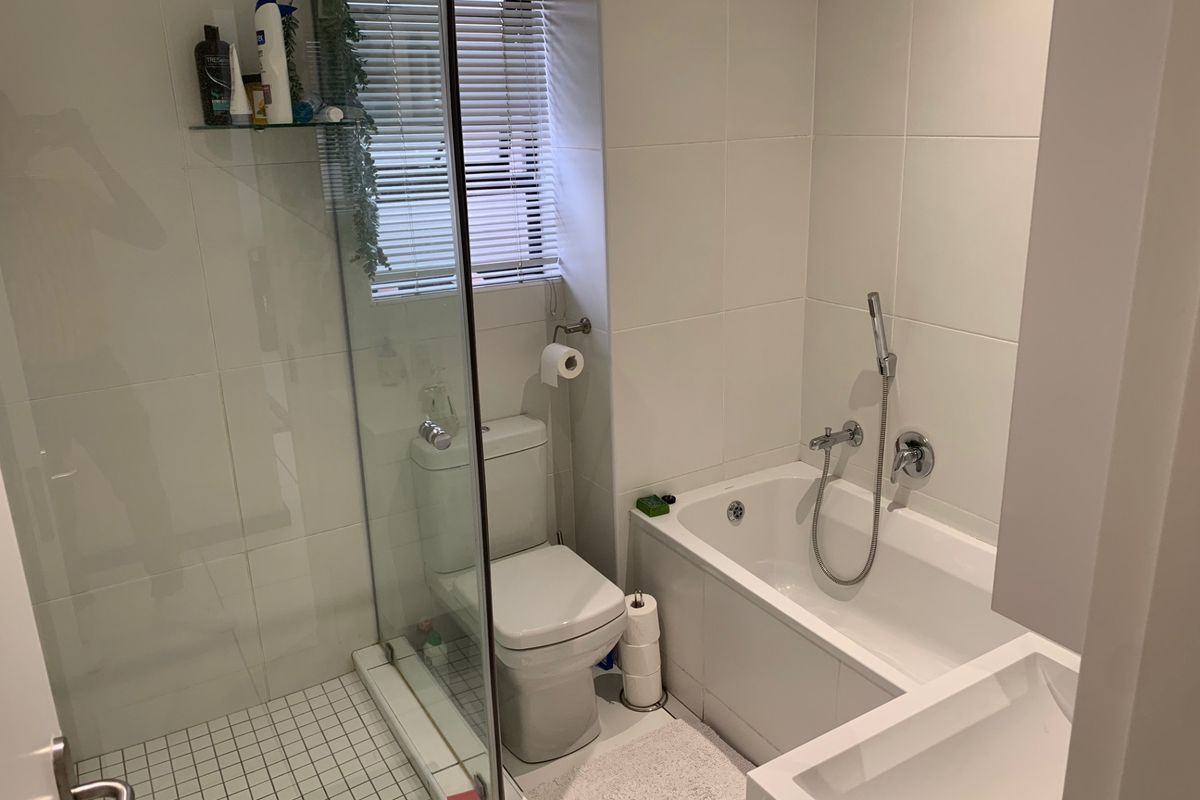 Modern bathroom featuring a glass-enclosed shower, a separate bathtub with handheld mixer, and neutral wall tiling.