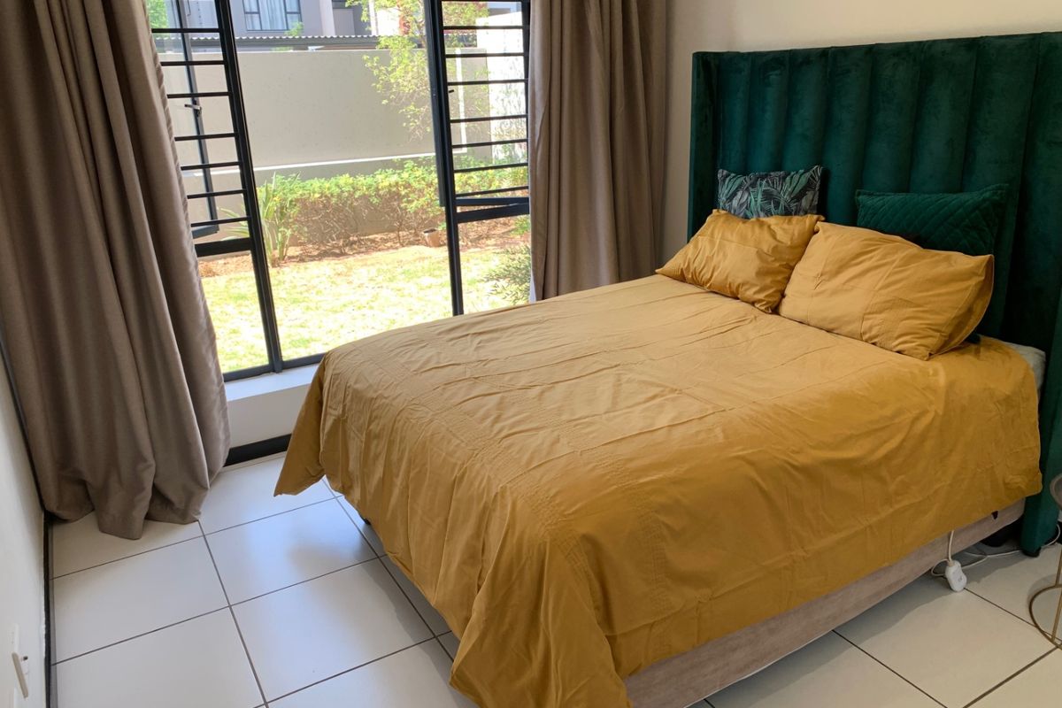 A well-lit bedroom featuring tiled flooring and a large window with security bars, offering a view of the exterior garden area.