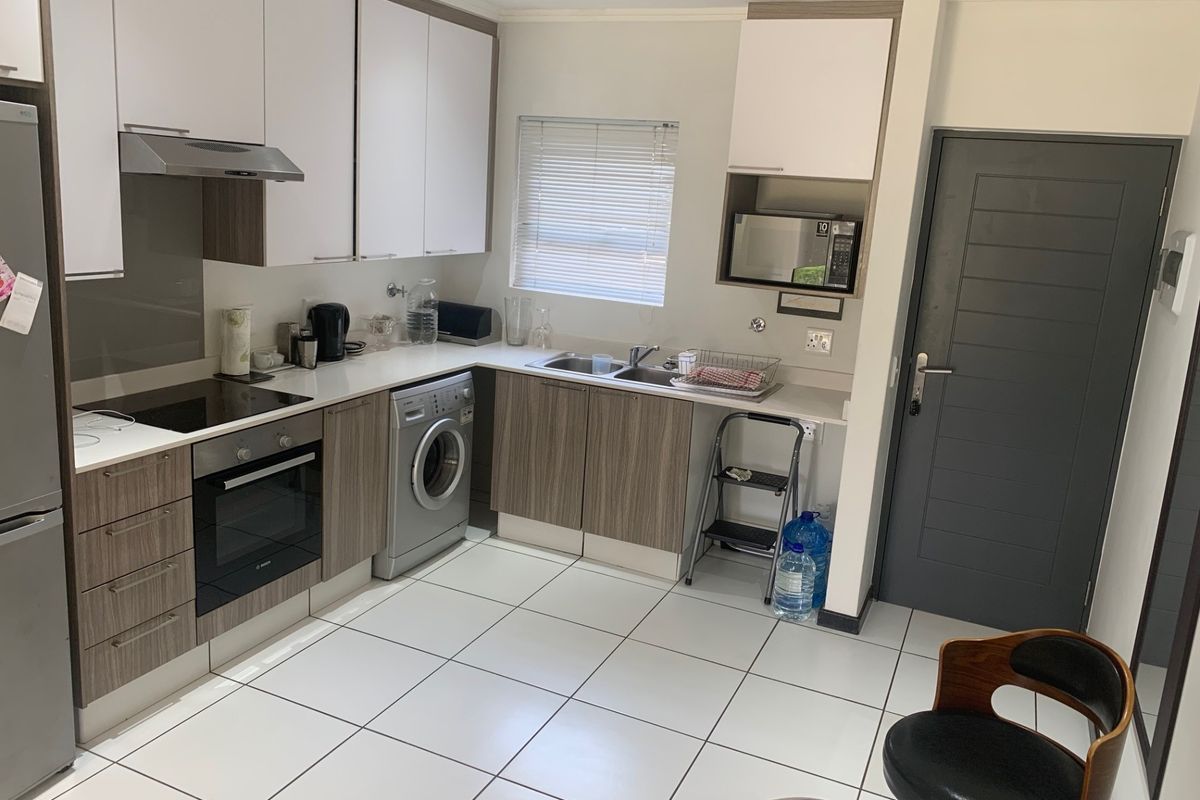 Modern kitchen featuring two-tone cabinetry, integrated oven and hob, stainless steel sink, and tiled flooring with convenient laundry plumbing connections.