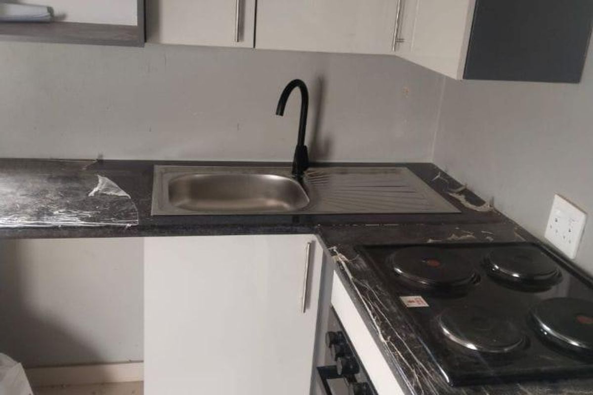 A compact kitchen featuring modern cabinetry, a black faucet, and integrated appliances. The space appears to be in the final stages of installation.