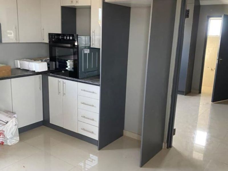 Modern kitchen featuring two-tone cabinetry, built-in oven, and sleek tiled flooring, offering a clean and functional space ready for final touches.