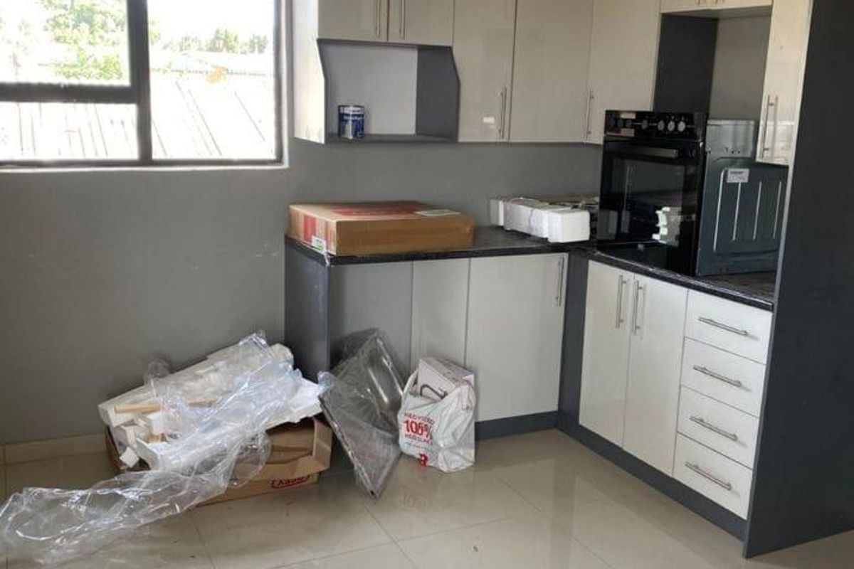 A modern, recently installed kitchen featuring sleek two-tone cabinetry, built-in oven, tiled flooring, and ample natural light from the side window.
