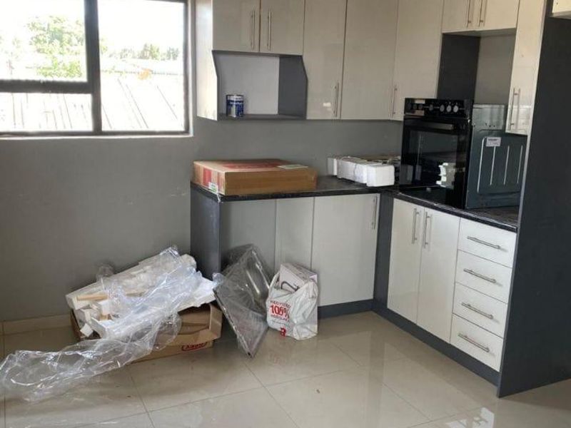 A modern, recently installed kitchen featuring sleek two-tone cabinetry, built-in oven, tiled flooring, and ample natural light from the side window.