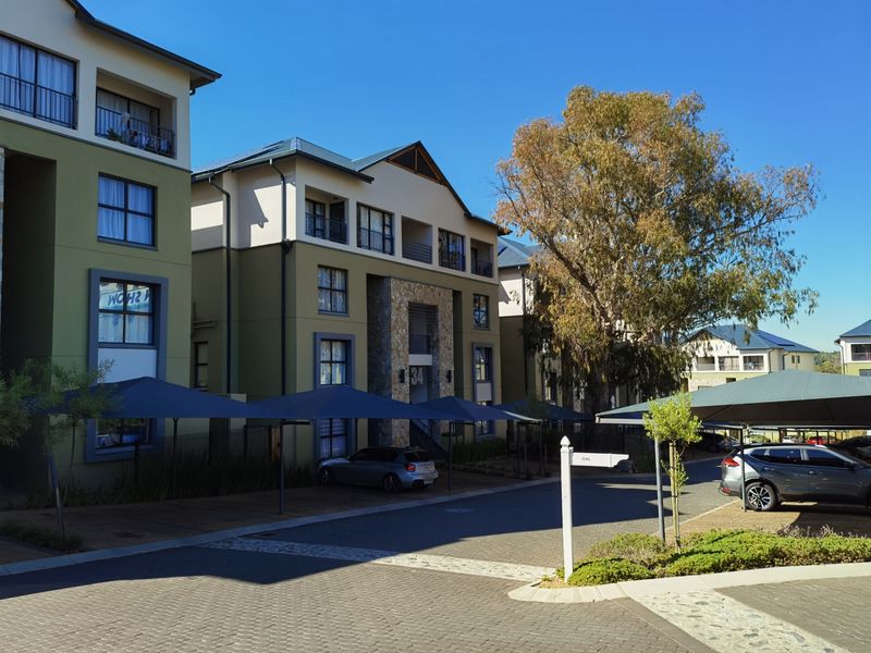 Exterior view of a modern apartment complex featuring stone facade accents, private balconies, and covered parking bays within a paved residential estate.