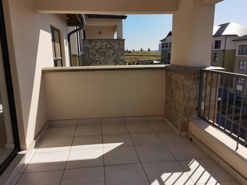 A covered balcony featuring tiled flooring, stone-clad pillars, and a metal balustrade, offering an open outdoor space for relaxation.