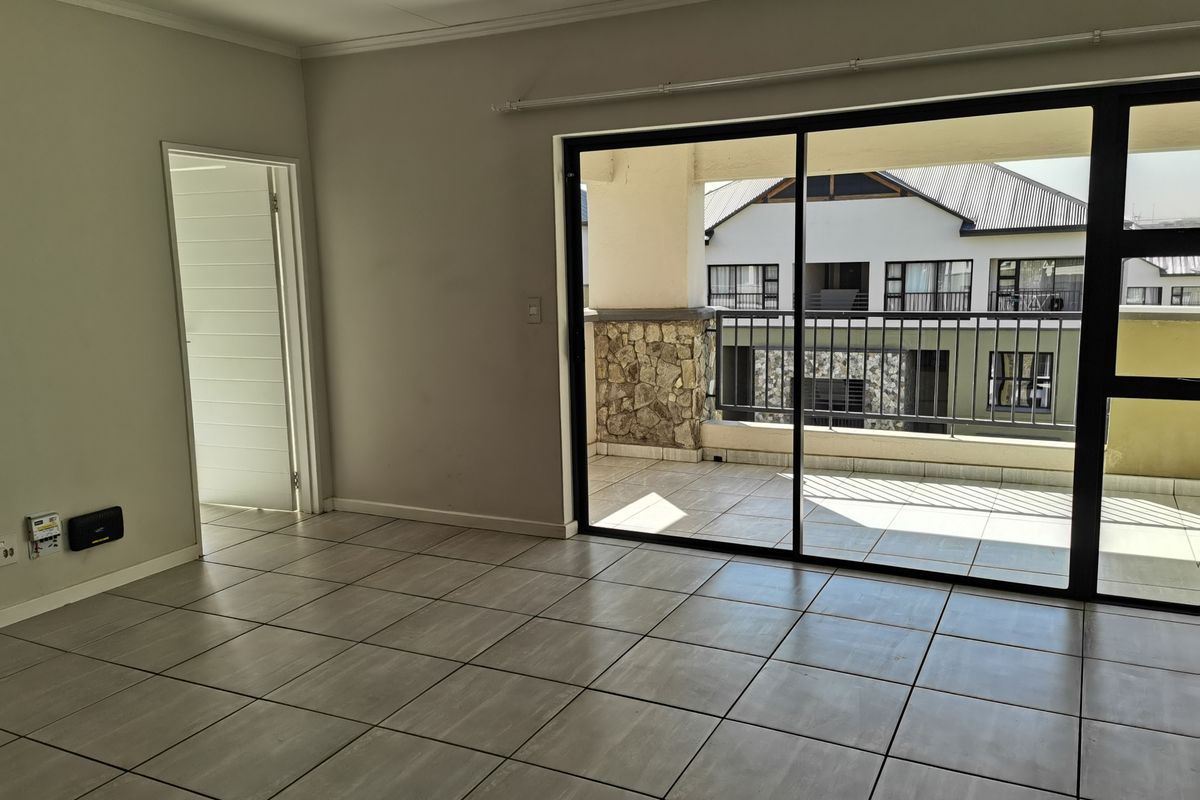An empty, tiled living room featuring large sliding glass doors that open onto a private balcony with stone accents and metal railings.