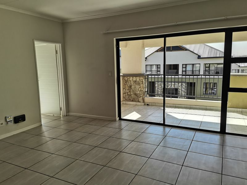 An empty, tiled living room featuring large sliding glass doors that open onto a private balcony with stone accents and metal railings.
