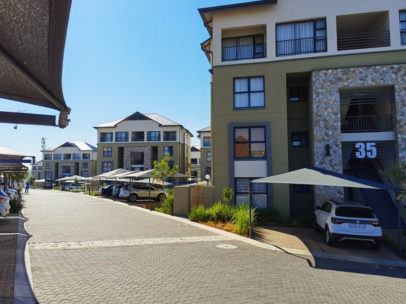 Exterior view of a modern apartment complex featuring paved driveways, covered parking bays, and multi-story residential buildings with stone cladding accents.