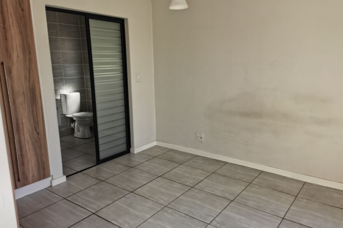 An empty bedroom featuring tiled flooring, a built-in wardrobe, and an en-suite bathroom with a sliding door entrance.