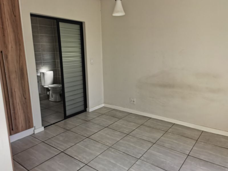An empty bedroom featuring tiled flooring, a built-in wardrobe, and an en-suite bathroom with a sliding door entrance.