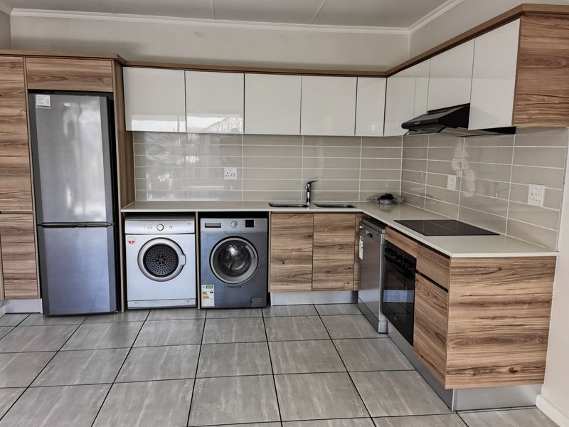 Modern kitchen featuring wood-grain and white high-gloss cabinetry, stone countertops, subway tile backsplash, and integrated appliances with neutral ceramic floor tiling.
