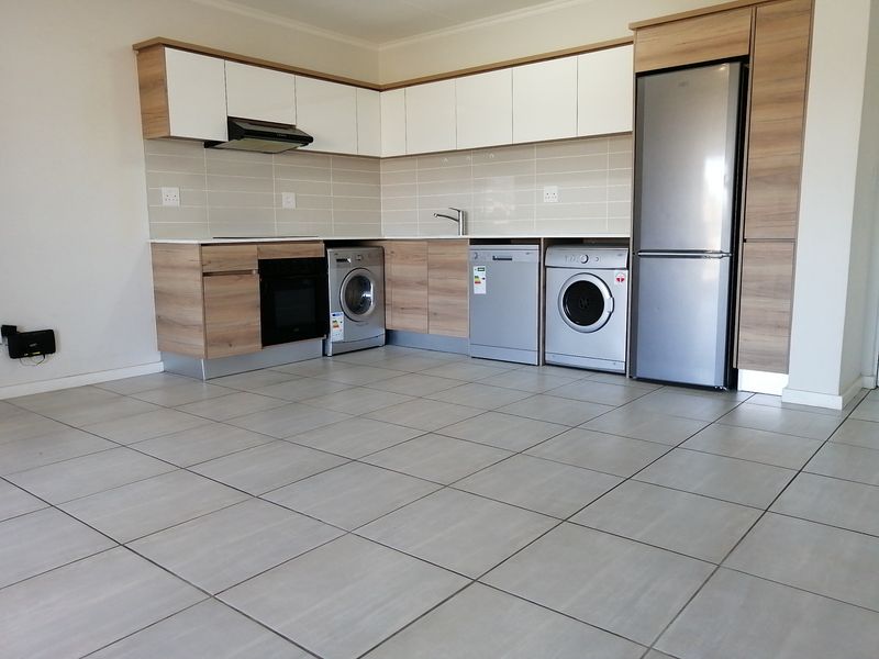 Modern open-plan kitchen featuring light wood-tone cabinetry, white upper cabinets, tiled backsplash, and integrated appliance spaces with neutral floor tiles.