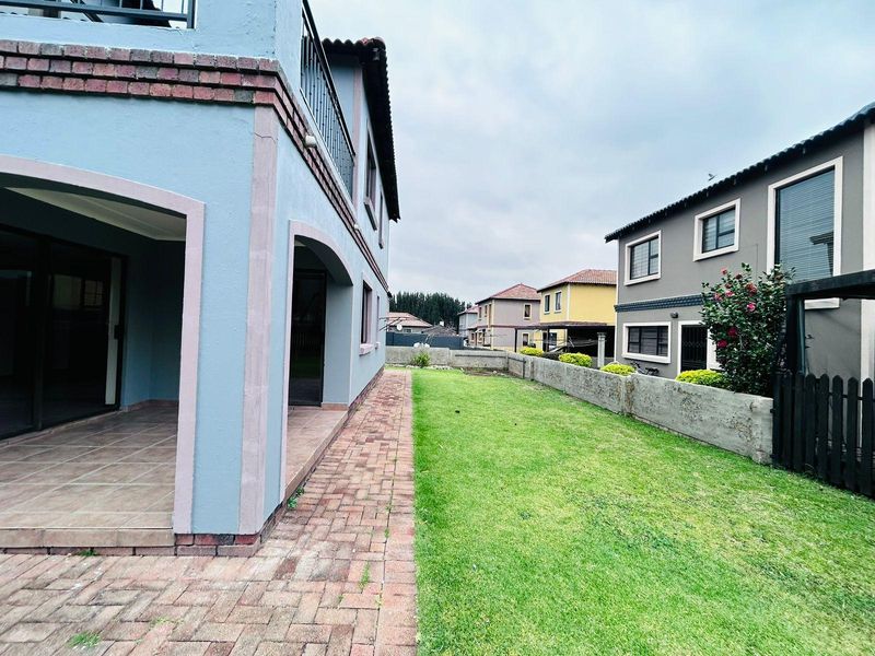 Rear view of the townhouse featuring a covered patio, brick paved walkway, and a private lawn area enclosed by a boundary wall.
