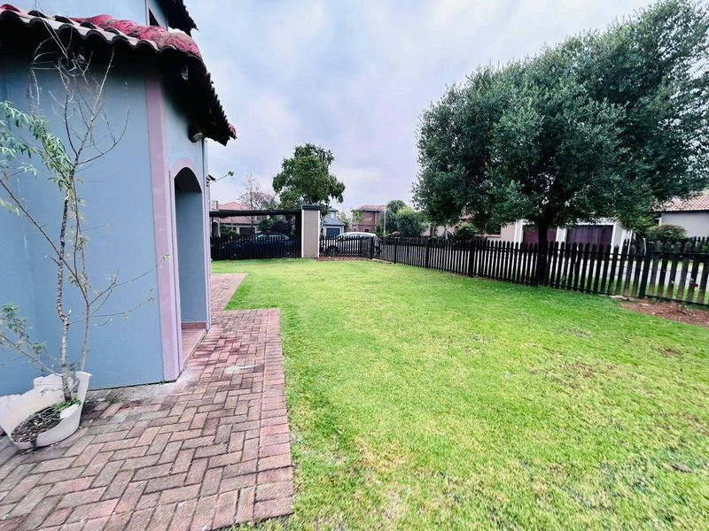 A private rear garden featuring a brick-paved patio area, a well-maintained lawn, and a perimeter picket fence.