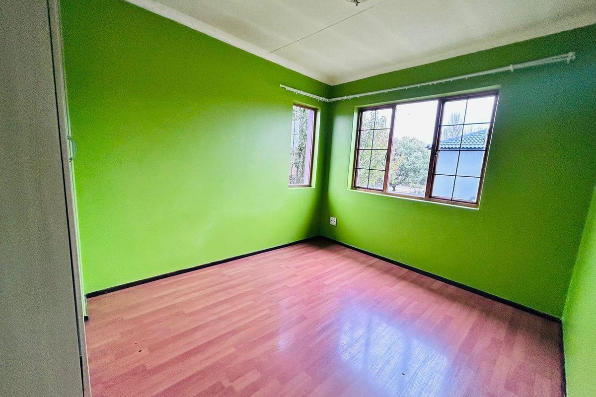 An empty bedroom featuring laminate flooring, built-in cupboards, and large windows providing natural light.