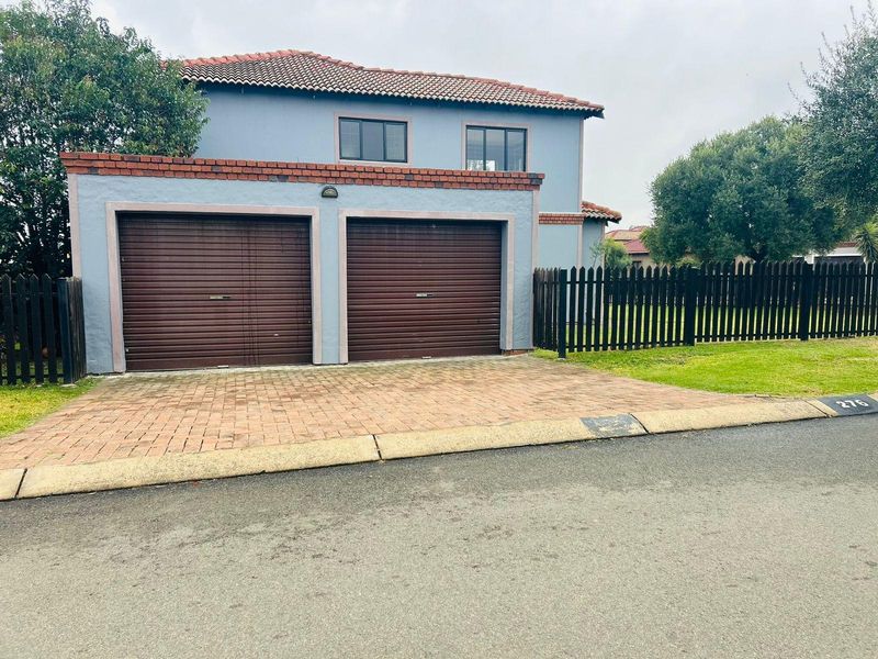 Front exterior view of a townhouse featuring a double garage, paved driveway, and perimeter picket fencing.