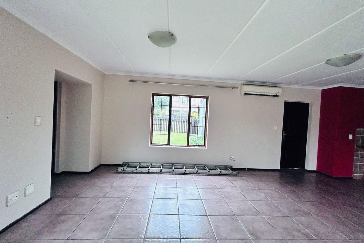 Spacious, empty living area featuring tiled flooring, an installed air conditioning unit, and natural light through a window with security bars.