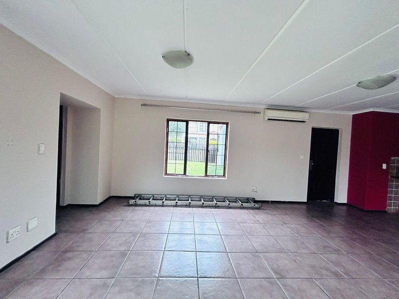 Spacious, empty living area featuring tiled flooring, an installed air conditioning unit, and natural light through a window with security bars.