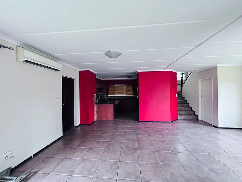 Spacious open-plan living area featuring tiled floors, a split-system air conditioner, and an integrated kitchen space with a staircase leading to the upper level.
