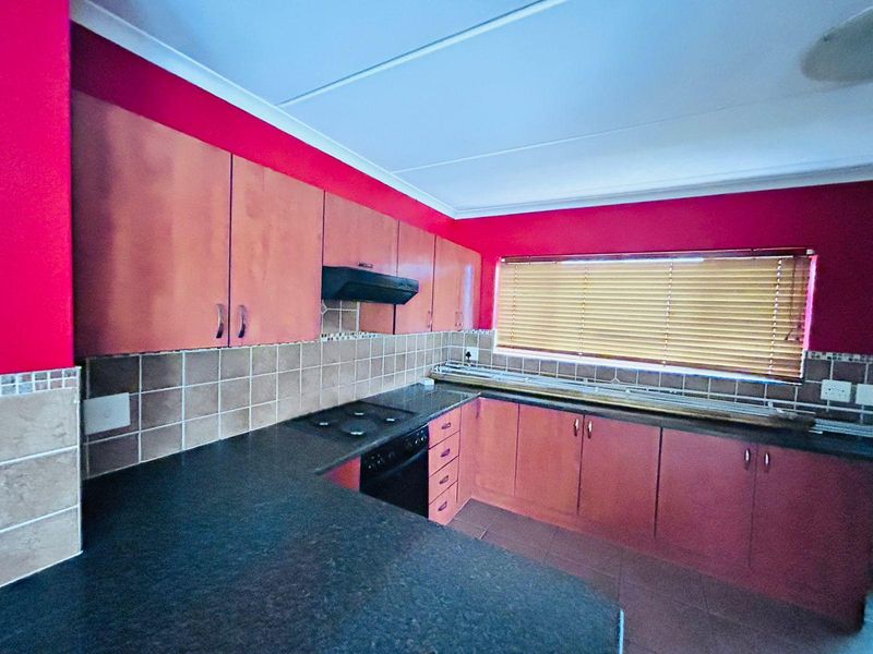 A functional kitchen featuring dark laminate countertops, built-in oven and hob, extractor fan, and ample cabinetry with a tiled backsplash.