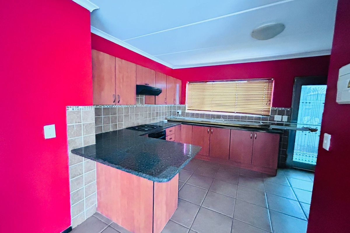 A functional kitchen featuring granite countertops, built-in wooden cabinetry, a hob with extractor fan, and tiled flooring.