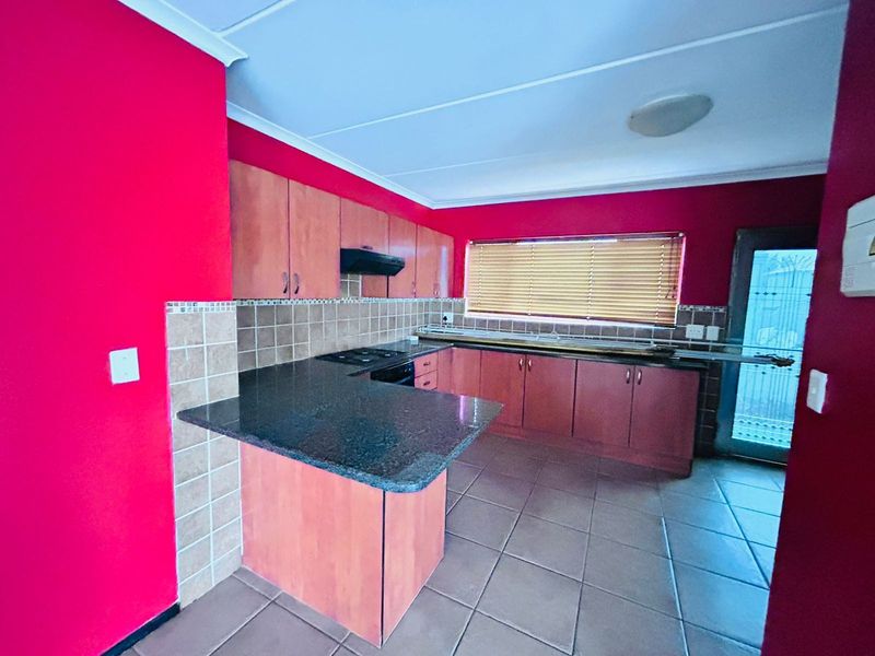A functional kitchen featuring granite countertops, built-in wooden cabinetry, a hob with extractor fan, and tiled flooring.
