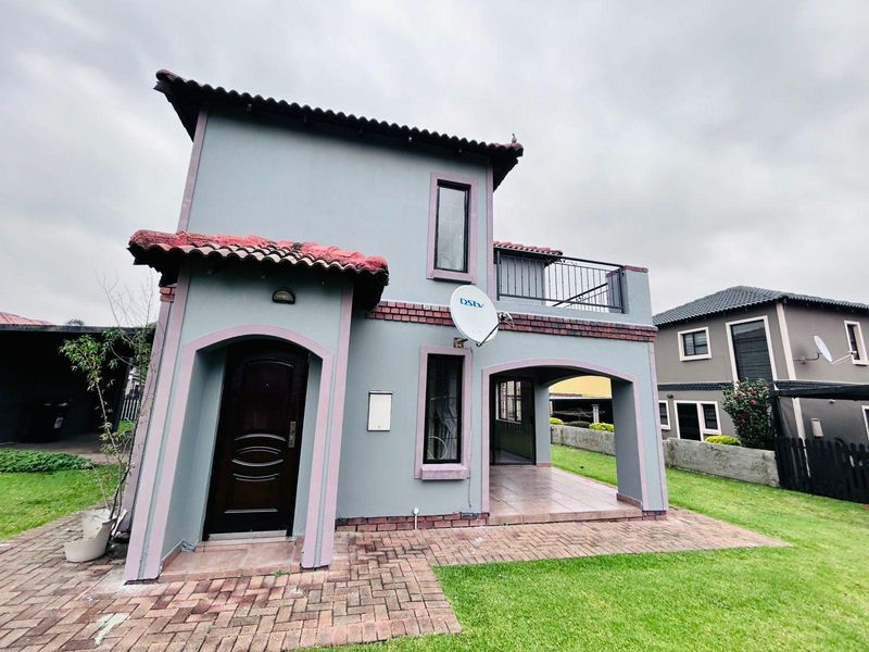 A two-story townhouse exterior featuring a covered patio, upper balcony, brick paving, and a tiled roof.