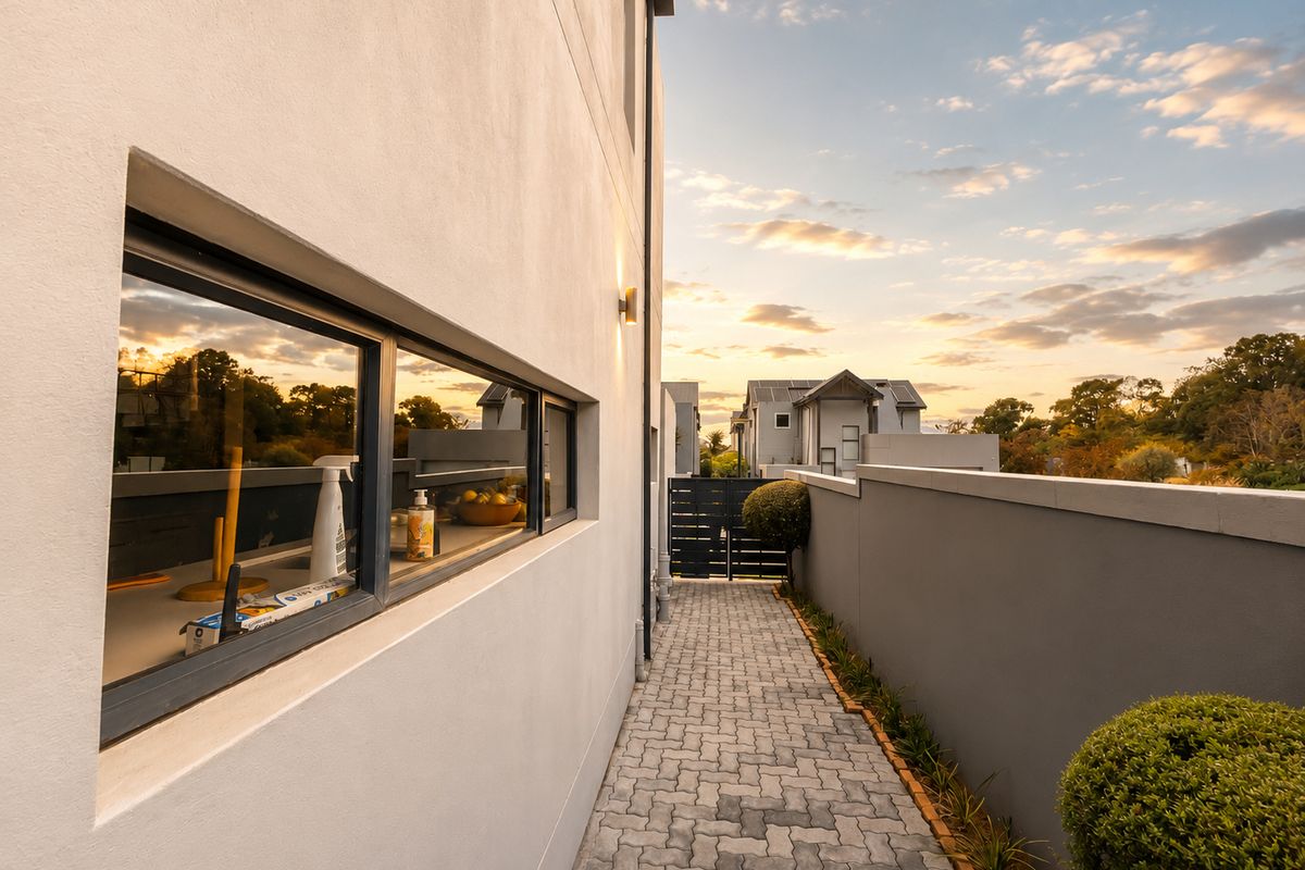 A well-maintained paved side walkway along the exterior of the property, featuring modern boundary walls and exterior lighting at sunset.