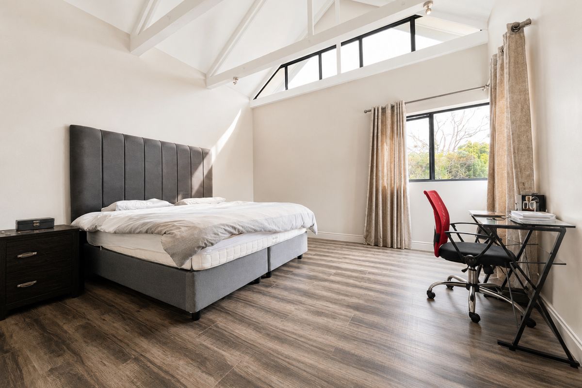 Spacious bedroom featuring high vaulted ceilings with exposed trusses, modern laminate flooring, and large windows providing ample natural light.