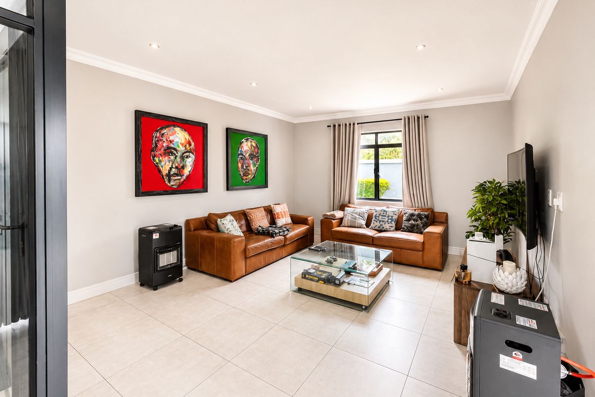A well-maintained living room featuring neutral tiled flooring, recessed downlighting, and elegant cornicing, providing a bright and comfortable space.
