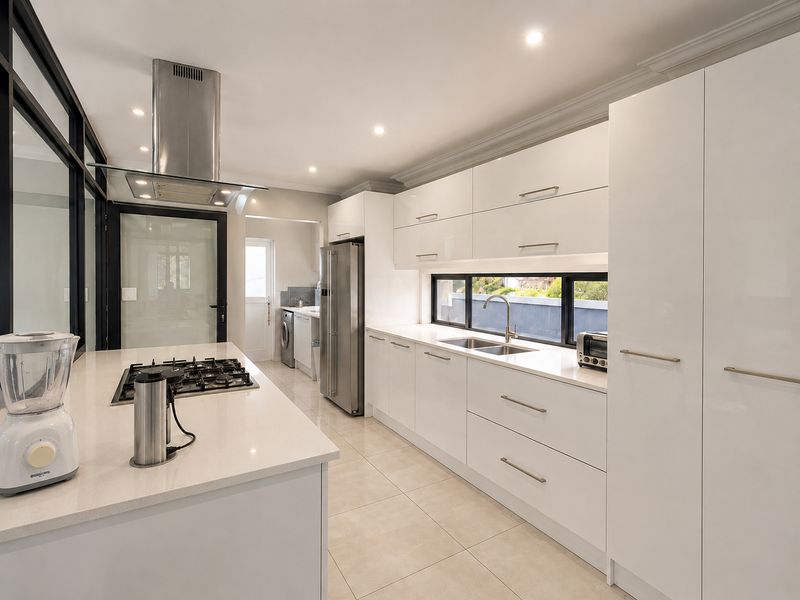 Modern kitchen featuring sleek white cabinetry, stone countertops, a gas hob with extractor fan, and a functional layout with an adjacent scullery area.