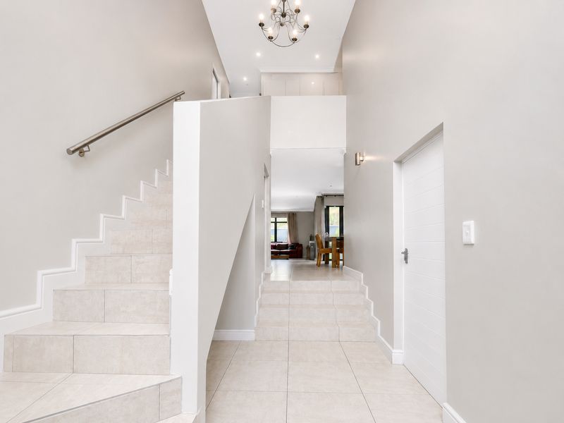 Spacious entrance hall featuring tiled flooring, a modern staircase with a stainless steel handrail, and elegant lighting fixtures leading into the open-plan living area.