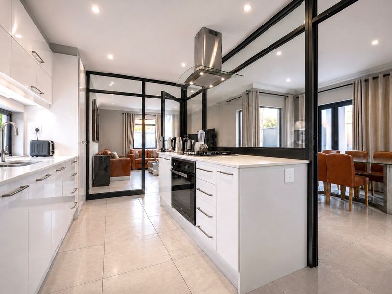 Modern kitchen featuring high-gloss white cabinetry, quartz countertops, integrated appliances, and stylish black-framed glass partitions separating the living and dining areas.