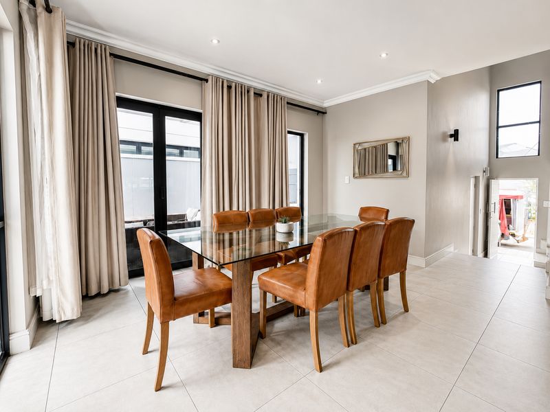 A bright and modern dining room featuring large format floor tiles, recessed lighting, and sliding glass doors leading to an outdoor area.